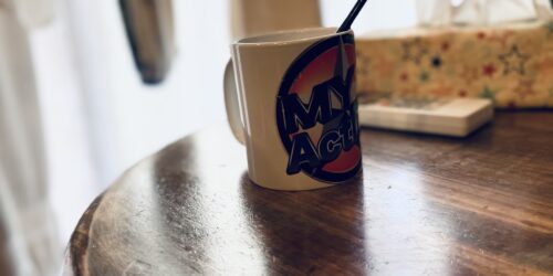机の上に、“My Action”のロゴがプリントされているマグカップが置いてある写真