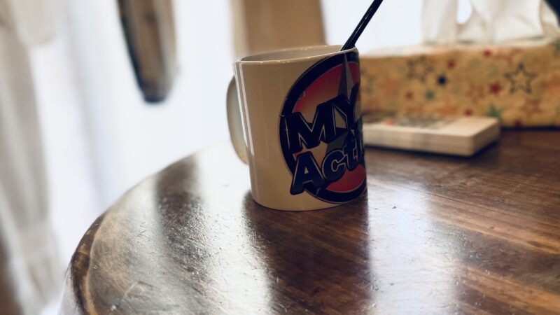 机の上に、“My Action”のロゴがプリントされているマグカップが置いてある写真